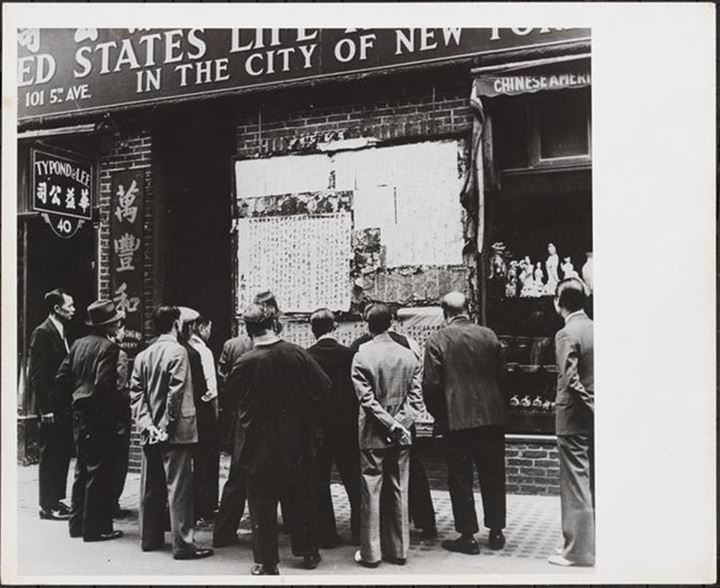 View of a crowd gathered around news bulletins in Chinese posted on a wall in Chinatown, 1944